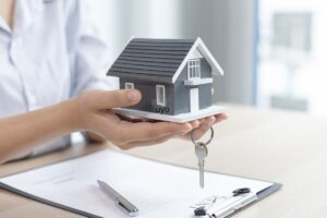 Persona che ha in mano una miniatura di una casa e delle chiavi