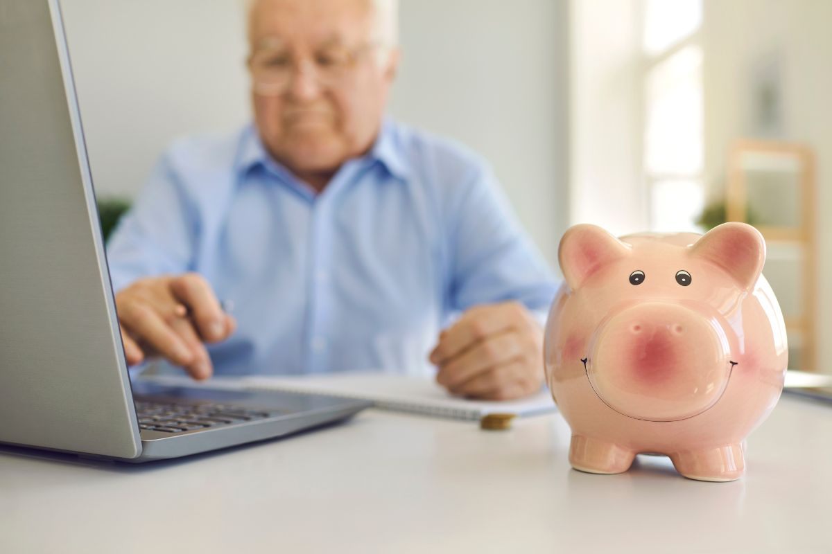 Pensionato che fa dei calcoli al computer e salvadanaio