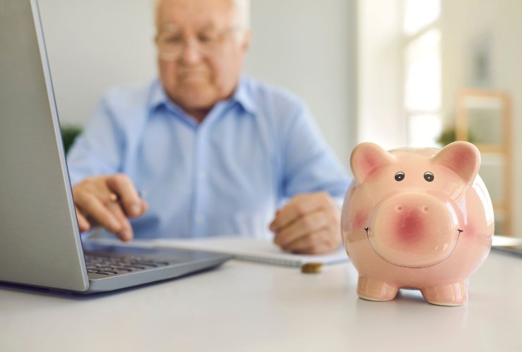 Pensionato che si informa e fa dei calcoli e salvadanaio